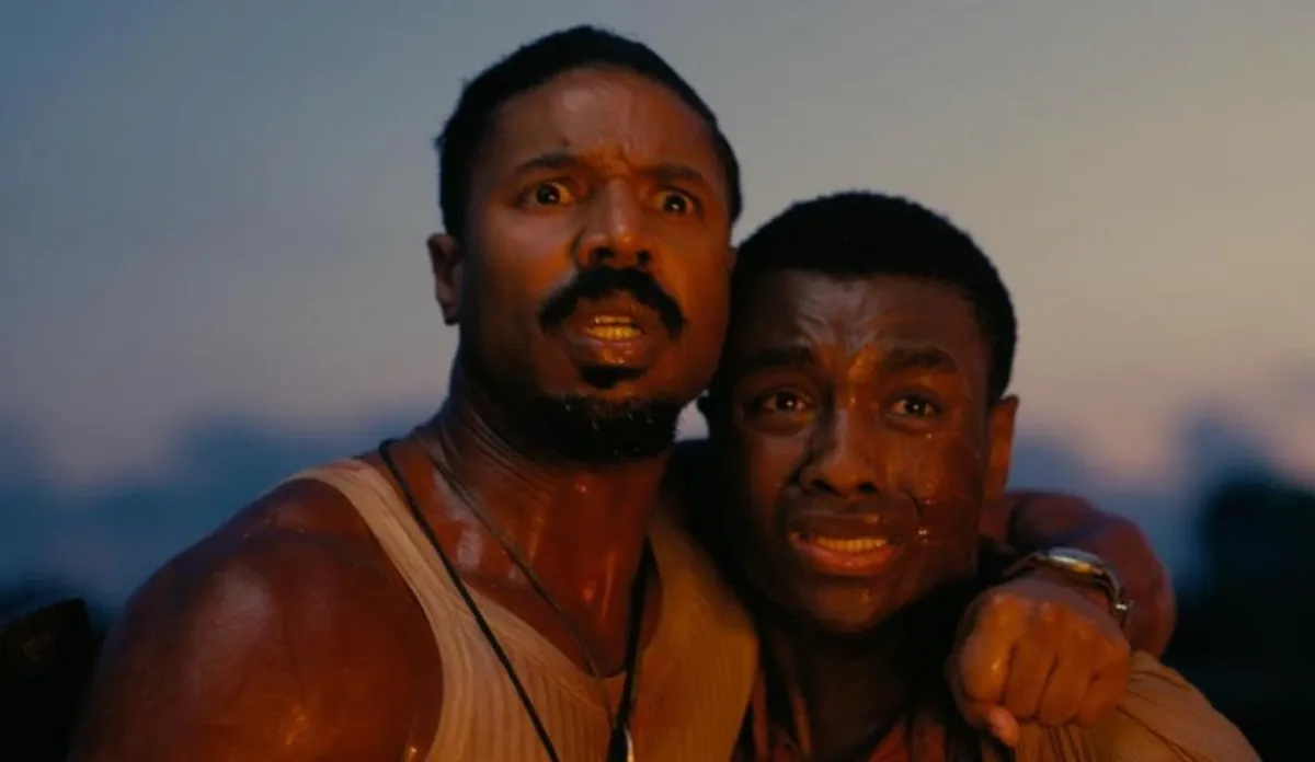 Michael B. Jordan ve Miles Caton, Günahkarlar 2025 filminden bu karede, Michael B. Jordan'ın kolu Miles Caton'ın omzundayken, ikisi de ter içinde, genişlemiş gözlerle dehşetle etrafa bakıyor ve gergin bir an yaşıyorlar.
