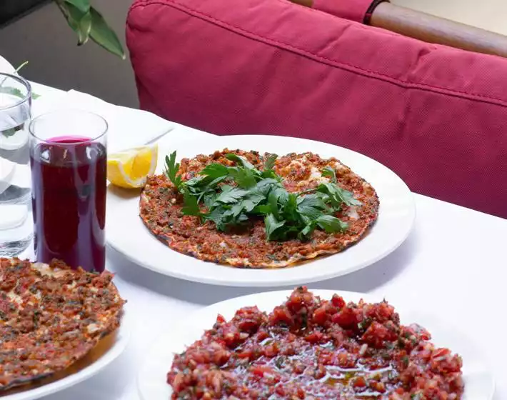 Oggusto Terminal Kadıköy Rehberi: Lezzet, Alışveriş ve Eğlence Durakları. Onur Kebap menüsünü temsil eden beyaz masada servis edilen taze lahmacunlar. Üzerinde maydanoz ve limon dilimi bulunan lahmacuna, bir bardak şalgam suyu ve lezzetli acılı ezme mezesi eşlik ediyor.