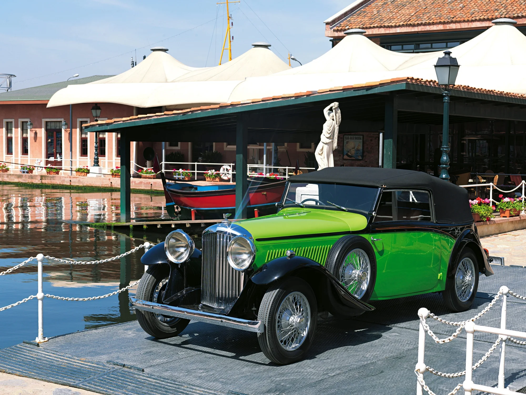 Rahmi Koç Müzesi'nde, su kenarındaki gri bir platformda duran, parlak yeşil ve siyah renkleriyle dikkat çeken, krom ızgaralı ve telli jantlı 1935 model üstü açık bir Bentley otomobil; arkasında beyaz tenteli binalar, kırmızı bir tekne ve yüksek bir sokak lambası görülüyor.