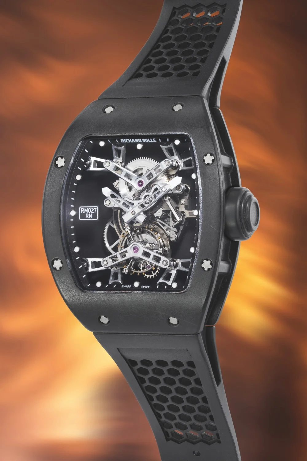 Bu resimde, tonneau kasa şekline sahip, kadranı iskeletleştirilmiş ve karmaşık tourbillon mekanizmasını açıkça gösteren, siyah kauçuk kayışı altıgen desenli, lüks bir Richard Mille RM 027 Tourbillon Nadal kol saati yakın çekim olarak görülmektedir.