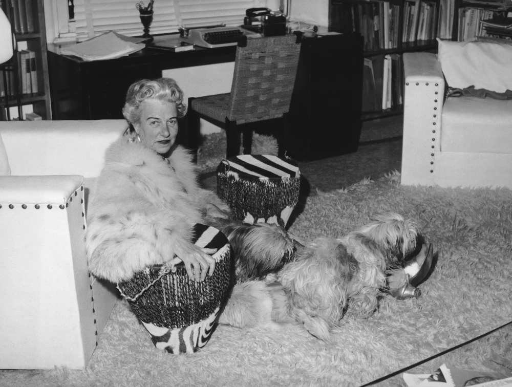 Siyah beyaz fotoğrafta, beyaz koltukta kürk mantosuyla kameraya bakmakta olan sanat koleksiyoncusu Peggy Guggenheim, bacaklarının arasında hasır ve püsküllü bir puf tutarken, kabarık tüylü köpeklerinden biri halının üzerinde uzanmış bir kaptan su içiyor, arka planda ise kitaplık dolu bir çalışma odası görülüyor.
