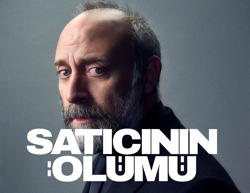 Halit Ergenç'in Satıcının Ölümü oyununun tanıtım görselinde, gri sakallı ve bıyıklı, mavi gözlü, düşünceli bir ifadeyle izleyiciye bakan yakın çekim portresi; görüntünün alt kısmında belirgin beyaz harflerle Satıcının Ölümü yazısı yer alıyor.