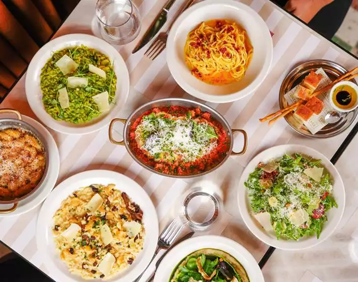 Oggusto Terminal Kadıköy Rehberi: Lezzet, Alışveriş ve Eğlence Durakları kapsamında sunulan gastronomi deneyimini yansıtan; çizgili masada sergilenen parmesanlı risotto, spagetti, fırın makarna, salata ve balzamik soslu focaccia ekmeğiyle donatılmış Trattoria Fontana İtalyan ziyafeti.