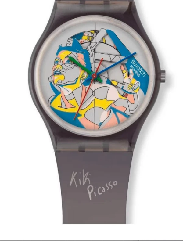Şeffaf gri kasası ve kayışıyla beyaz bir arka plan üzerinde yer alan Swatch Kiki Picasso koleksiyonundan bir kol saati, kadranında mavi, sarı ve pembe tonlarında, soyut ve kübist bir sanatçının tarzını yansıtan, yukarı bakan bir kadın portresi ve kayışında Kiki Picasso imzasıyla dikkat çekiyor.