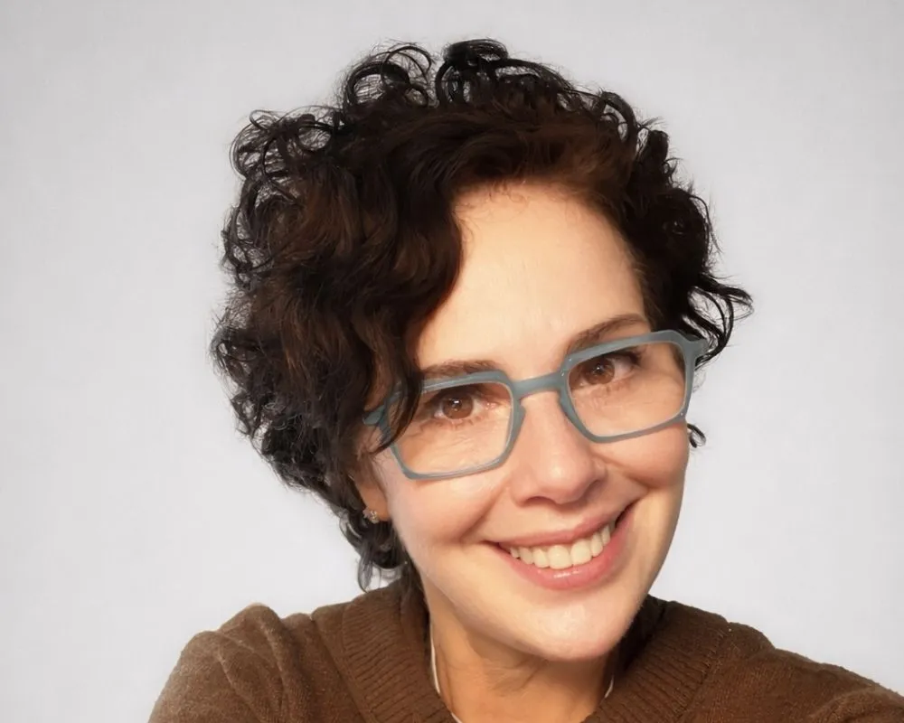 Filmlerdeki yapımcı kimliğiyle bilinen Zeynep Atakan'ın, kıvırcık kısa saçları, açık renk kare gözlükleri ve içten gülümsemesiyle yakın çekim portresi, sinema dünyasına kattığı değeri ve uluslararası ödüllerle tescillenmiş başarılarını yansıtıyor.