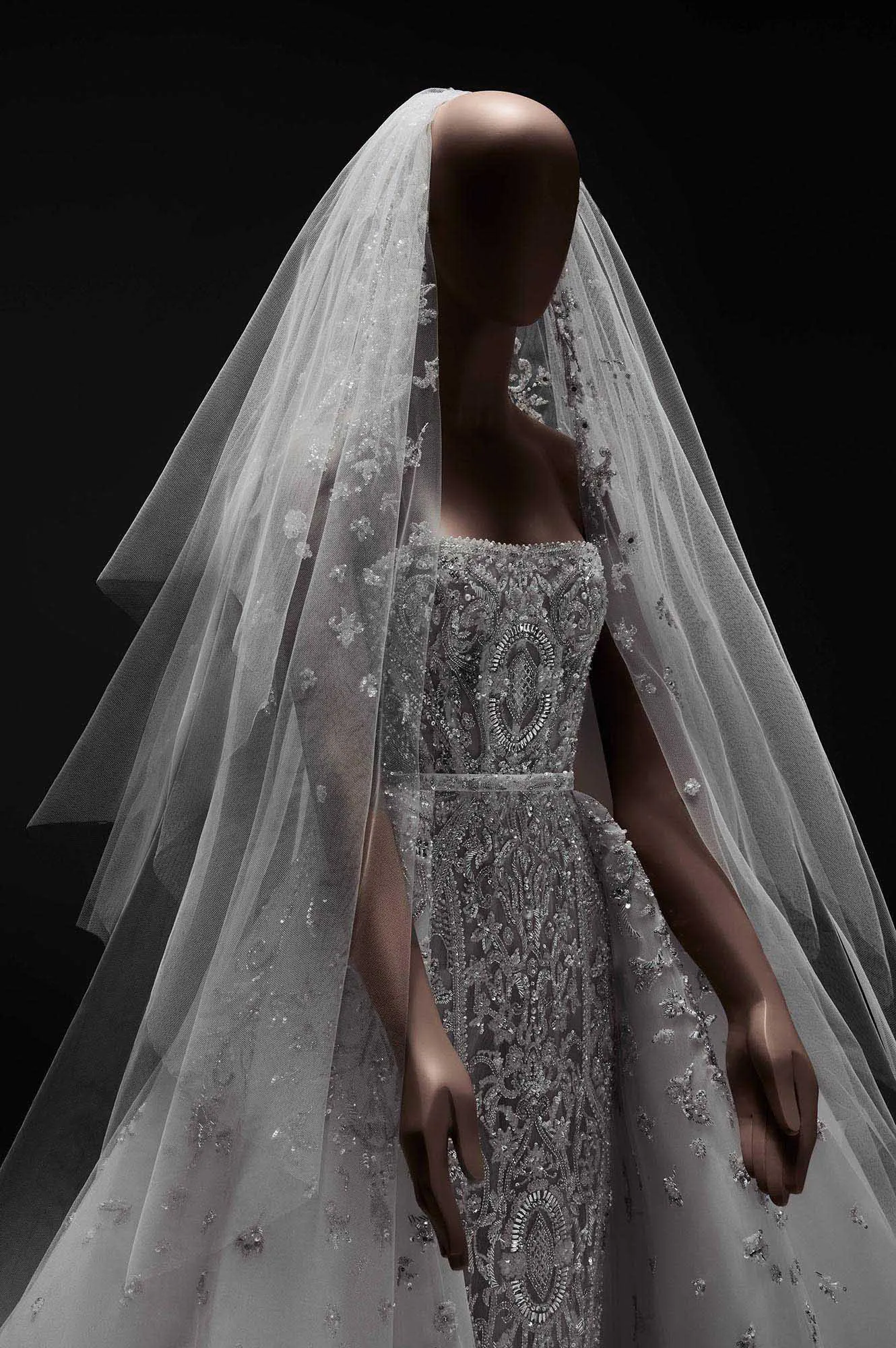 Zuhair Murad'ın ışıltılı gelinlik koleksiyonundan bir parça sergileyen, couture işçiliğiyle detaylandırılmış, straplez üst kısmı ve yoğun gümüş işlemeleriyle göz kamaştıran prenses siluet bir gelinlik, uzun ve zarif işlemeli duvağıyla modern romantizmi kusursuzca yansıtıyor.