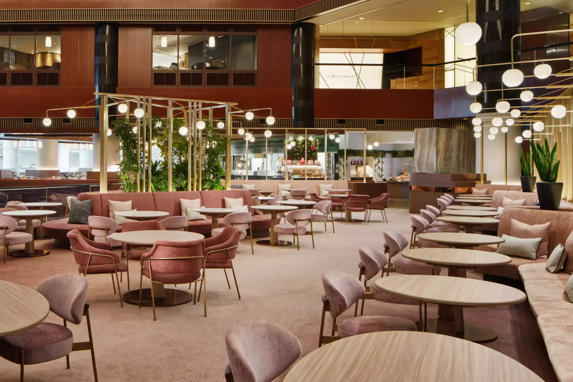 Modern ve zarif bir atmosfer sunan Atrium Lounge'da, kadife dokulu pembe tonlarındaki rahat koltuklar ve bej renkte ahşap yuvarlak masalar geniş alana yayılmıştır. Tavandan sarkan küresel beyaz lambalar ve yeşil bitkilerle aydınlatılan mekan, sıcak ve davetkar bir his vermektedir.