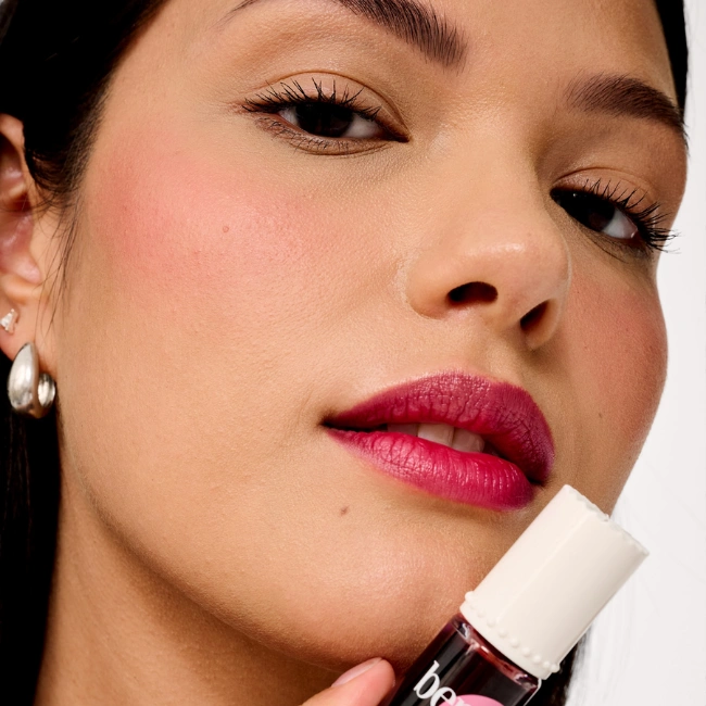 Yanaklarında taze pembe allık ve dudaklarında canlı mürdüm tonuyla doğal bir ışıltıya sahip model, Benefit Cosmetics Benetint'i tutarak ürünün yanak ve dudaklara verdiği kalıcı renk etkisini çarpıcı bir şekilde sergiliyor.