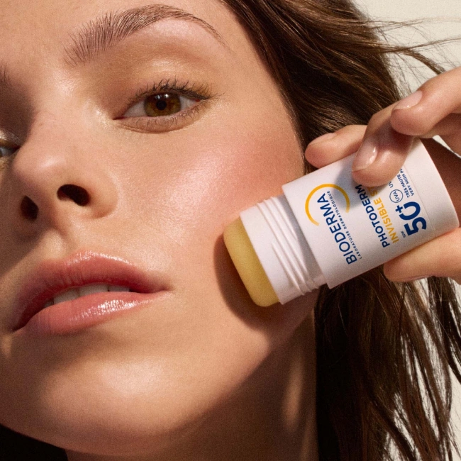 Doğal güzelliği ve parlak cildiyle dikkat çeken genç bir kadın, güneşin olumsuz etkilerinden güçlü bir koruma sağlamak amacıyla Bioderma Photoderm Invisible SPF 50+ stick güneş kremini yüzüne, özellikle yanağına nazikçe uygulayarak pratik bir cilt bakım anını sergiliyor.