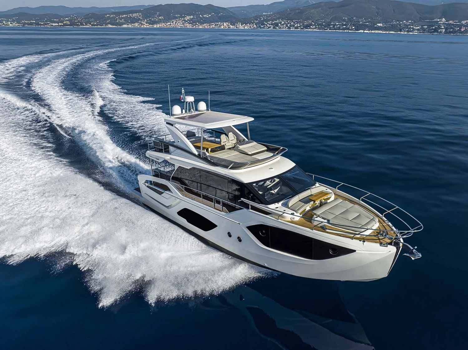 Mavi denizde hızla yol alarak arkasında beyaz köpüklü bir iz bırakan, flybridge'li ve şık tasarımlı beyaz Absolute 52 Fly yatı, Singapur Yat Fuarı'nda tanıtılan modern ve lüks deniz araçlarının görkemini gözler önüne seriyor.