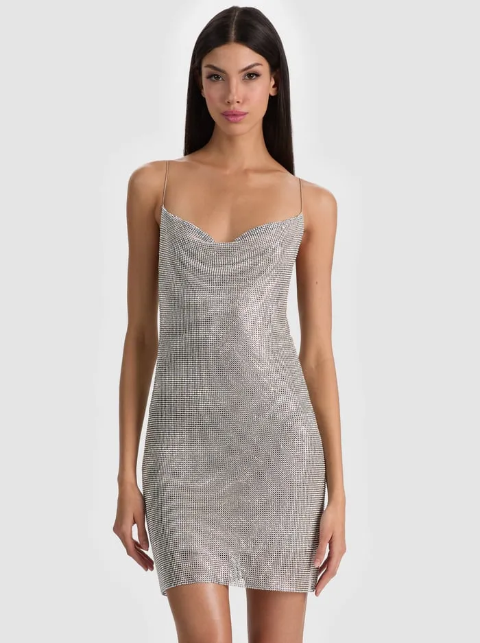 Model, ince ip askılı ve dökümlü yakalı, gümüş rengi, tamamen ışıltılı ve parlak mini bir after party elbisesi giyerek, düğün sonrası kutlamalar için göz alıcı tasarımların parıltılı ve iddialı trendini sergiliyor.