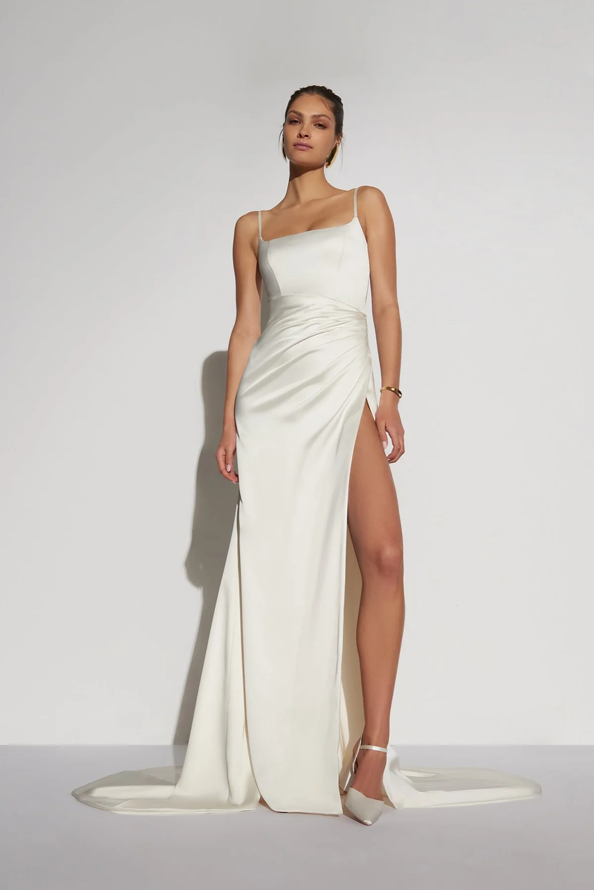 Minimalist şıklığı temsil eden bu 2026 after party elbisesi modeli, ince askılı, kare yakalı ve sol bacağında yüksek bir yırtmaç bulunan fildişi rengi saten kumaşıyla dikkat çekiyor, zarafetinden ödün vermeden dans etmek isteyen gelinler için ideal bir tercih sunuyor.