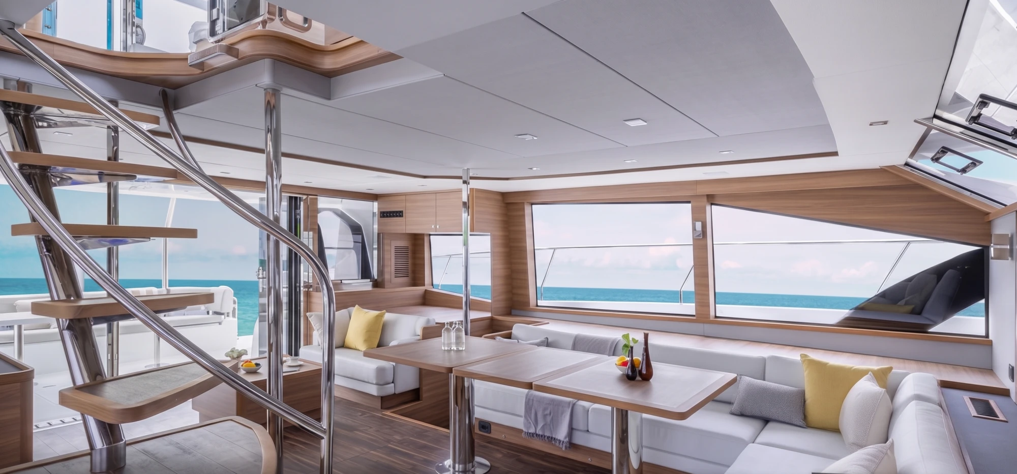 Deniz manzaralı geniş pencerelere sahip bu Aquila 54 katamaran motoryatın iç mekanında, beyaz konforlu koltukların ve ahşap masaların bulunduğu şık salon ile arkada görünen mutfak alanı, lüks ve aydınlık bir yaşam alanı sunuyor.