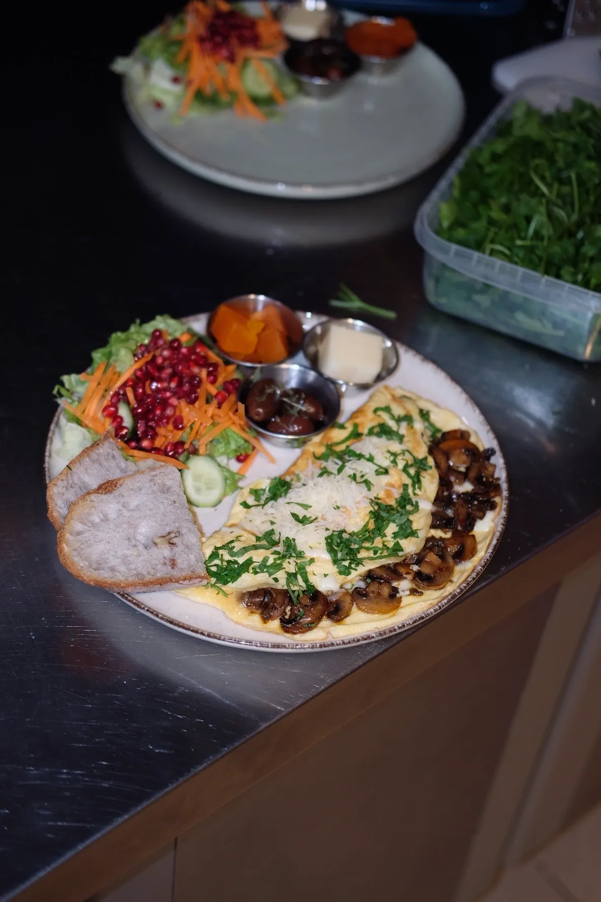 Ankara'daki Bala Bakehouse'ta sunulan, bol mantarlı, rendelenmiş peynir ve taze maydanozla zenginleştirilmiş bir omlet, nar, havuç, marul ve salatalık dilimleriyle hazırlanan canlı bir salata, dilimlenmiş artisan ekmek, tereyağı, zeytin ve ev yapımı kayısı reçeli gibi lezzetlerle dolu doyurucu bir kahvaltı tabağı.