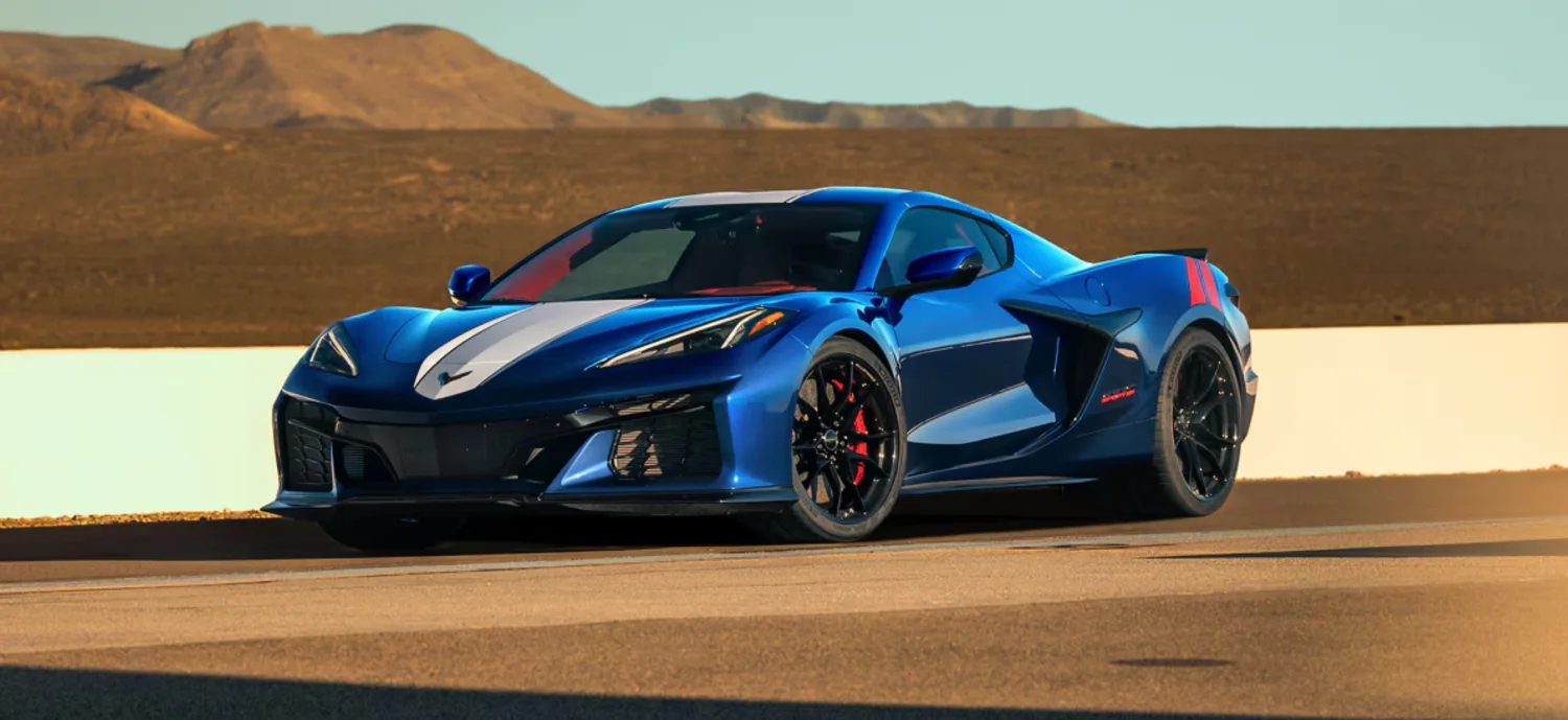 Çöl manzarasının önünde, kaputundan tavanına uzanan beyaz şeritli, yanlarında kırmızı Grand Sport çizgileri olan parlak mavi bir Chevrolet Corvette Grand Sport, siyah jantları ve kırmızı fren kaliperleriyle asfaltta duruyor.