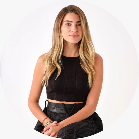 Uzun dalgalı sarı saçları, şık siyah crop top ve pileli pantolon kombiniyle oturan Gaios markasının kurucusu Dilan Can, modern bir stil sunumuyla 2026/2027 gelin saçı aksesuarları trendleri ve gelinlik dünyasındaki yenilikleri ele alan bu yazıya katkıda bulunuyor.