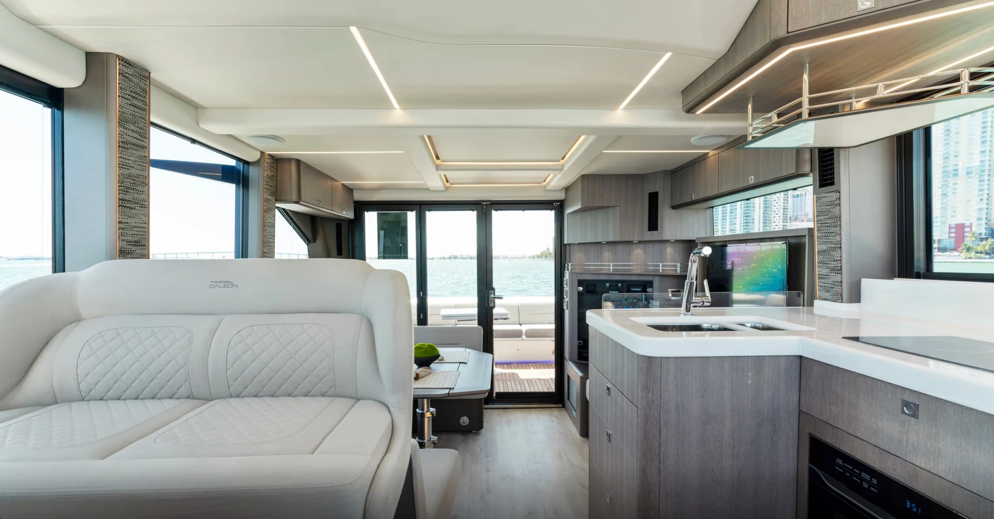 Galeon 440 Fly yatının iç mekanı, modern ve lüks bir tasarıma sahip geniş salonu ve tam donanımlı mutfak alanını gösteriyor; geniş pencerelerden görünen deniz ve şehir manzarasıyla ferah bir ortam sunuyor.