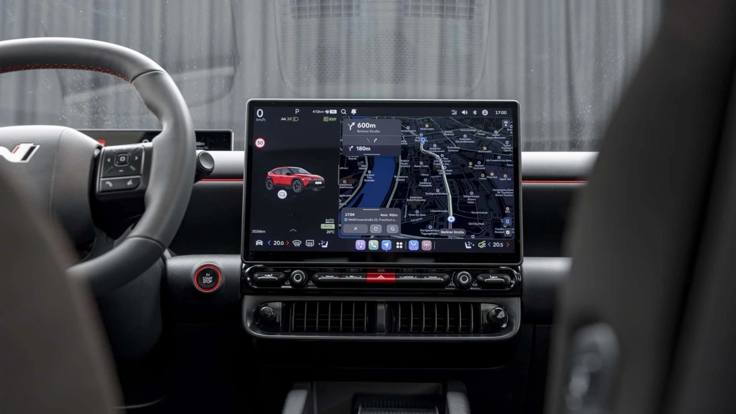 Hyundai Ioniq 3'ün iç mekanında konumlanmış büyük multimedya ekranı, üzerinde kırmızı bir araç simgesiyle güncel konumu, 412 km menzil bilgisi ve detaylı yol tariflerini gösteren harita tabanlı navigasyon uygulamasını sergilerken, ekranın altında klima kontrol düğmeleri ve havalandırma ızgaraları, sol yanda ise sportif direksiyon simidi ve kırmızı başlat/durdur düğmesi belirgin şekilde görülüyor.