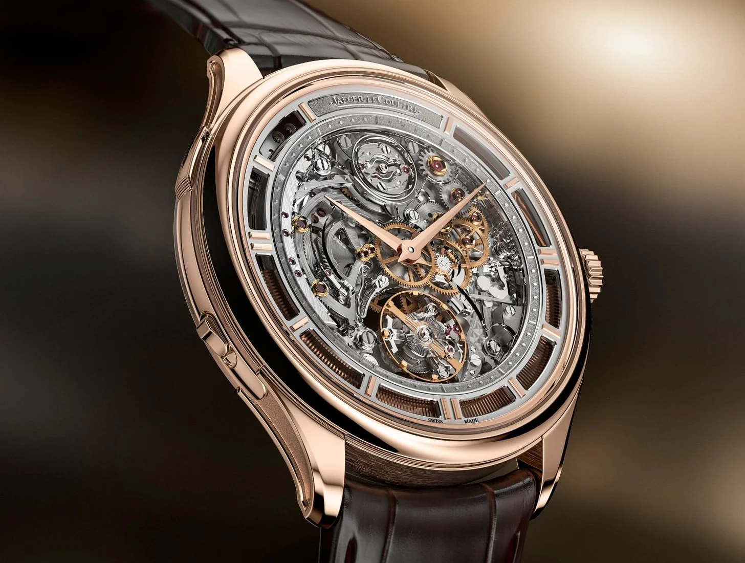 Jaeger-LeCoultre Master Hybris Mechanica Ultra-Thin Tourbillon saatinin gül altın kasası ve kahverengi timsah derisi kayışı net bir şekilde görülürken, karmaşık iskelet kadranı içerisindeki hassas tourbillon mekanizmasını ve altın rengi dişlilerle dolu mühendislik harikası iç yapısını gözler önüne seriyor.