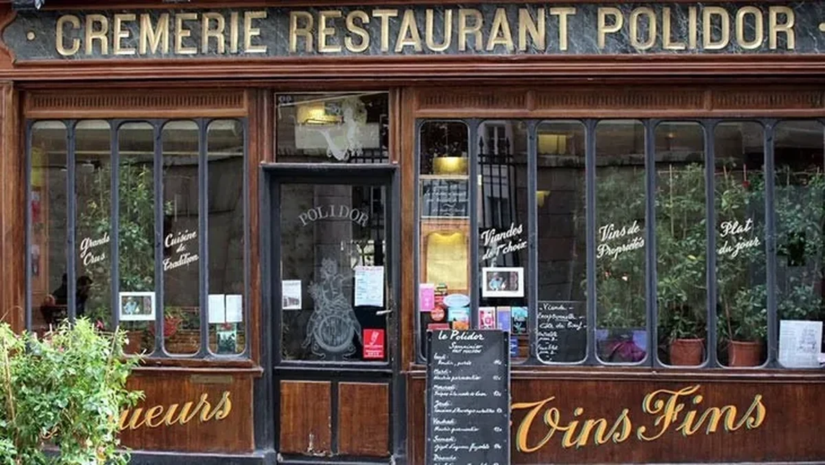 Midnight in Paris filminde geçen ünlü restoran Le Polidor'un, ahşap çerçeveli büyük cam pencereleri ve üst kısmında CREMERIE RESTAURANT POLIDOR yazan tabelasıyla geleneksel Fransız brasserie ruhunu yansıtan ön cephesi görülüyor.