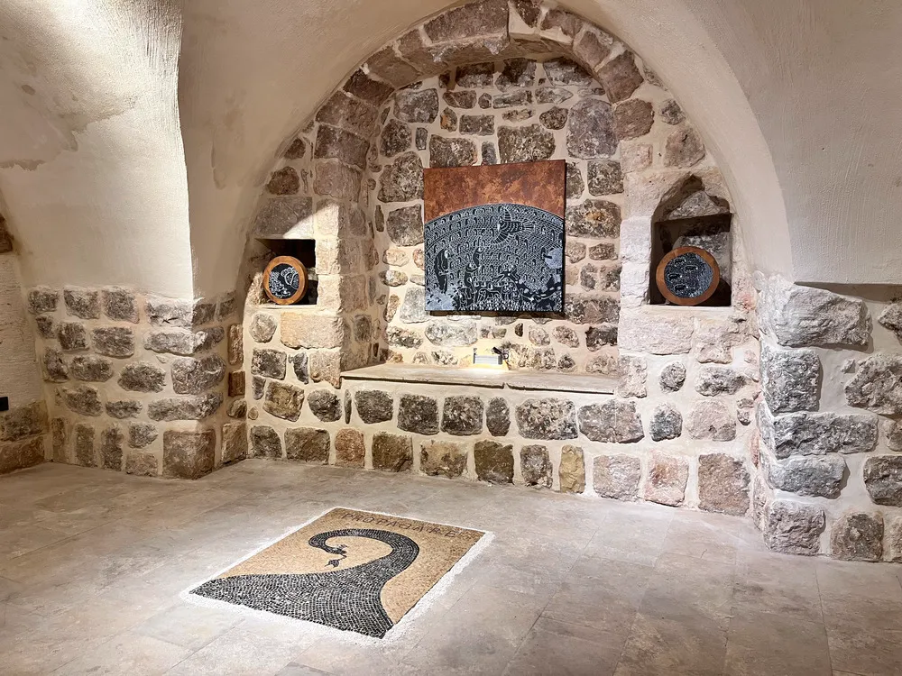 Mardin Bienali Eşik Sergisi'ne ev sahipliği yapan taş kemerli, yüksek tavanlı galerimizde, ortada koyu renkli ve kahverengi tonlarda soyut desenli büyük bir tablo, yan nişlerde ayna benzeri dairesel iki eser ve yerde PROPAGANDA yazısı ile dalgalı bir mozaik halı sergileniyor.