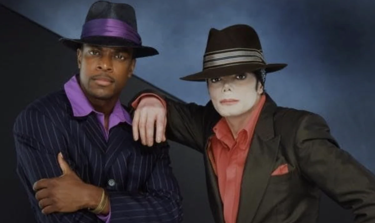 Chris Tucker ile, You Rock My World videosuyla ilişkilendirilen ikonik fötr şapkaları ve şık takım elbiseleriyle yan yana poz veriyor; Chris Tucker lacivert çizgili takım elbisesi ve mor gömleğiyle, Michael Jackson ise koyu renk takımı ve kırmızı gömleğiyle kameraya bakıyor.