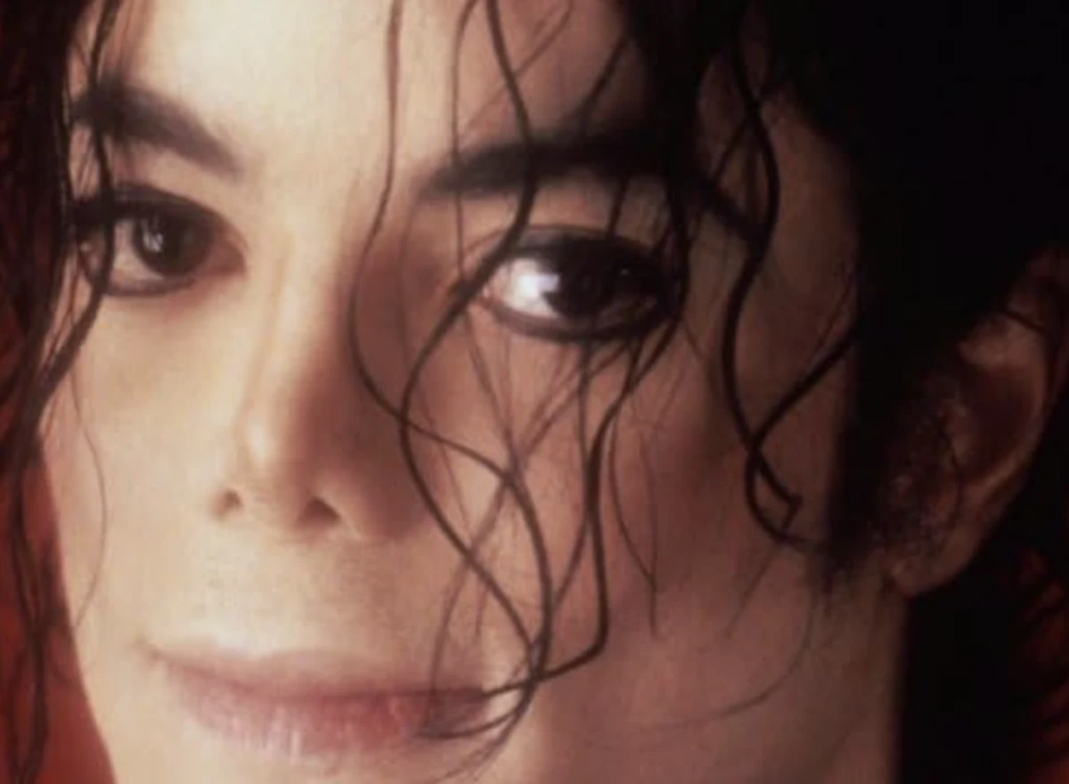 Michael Jackson'ın gözlerinin doğrudan izleyiciye baktığı, yüzünün nemli görünen kıvırcık saç telleriyle kısmen örtüldüğü, kırmızımsı bulanık bir arka plan önünde çekilmiş bu yakın portre, onun kamuoyunda tartışılan hayatını ve 'true crime' konularıyla olan karmaşık ilişkisini çağrıştırıyor.