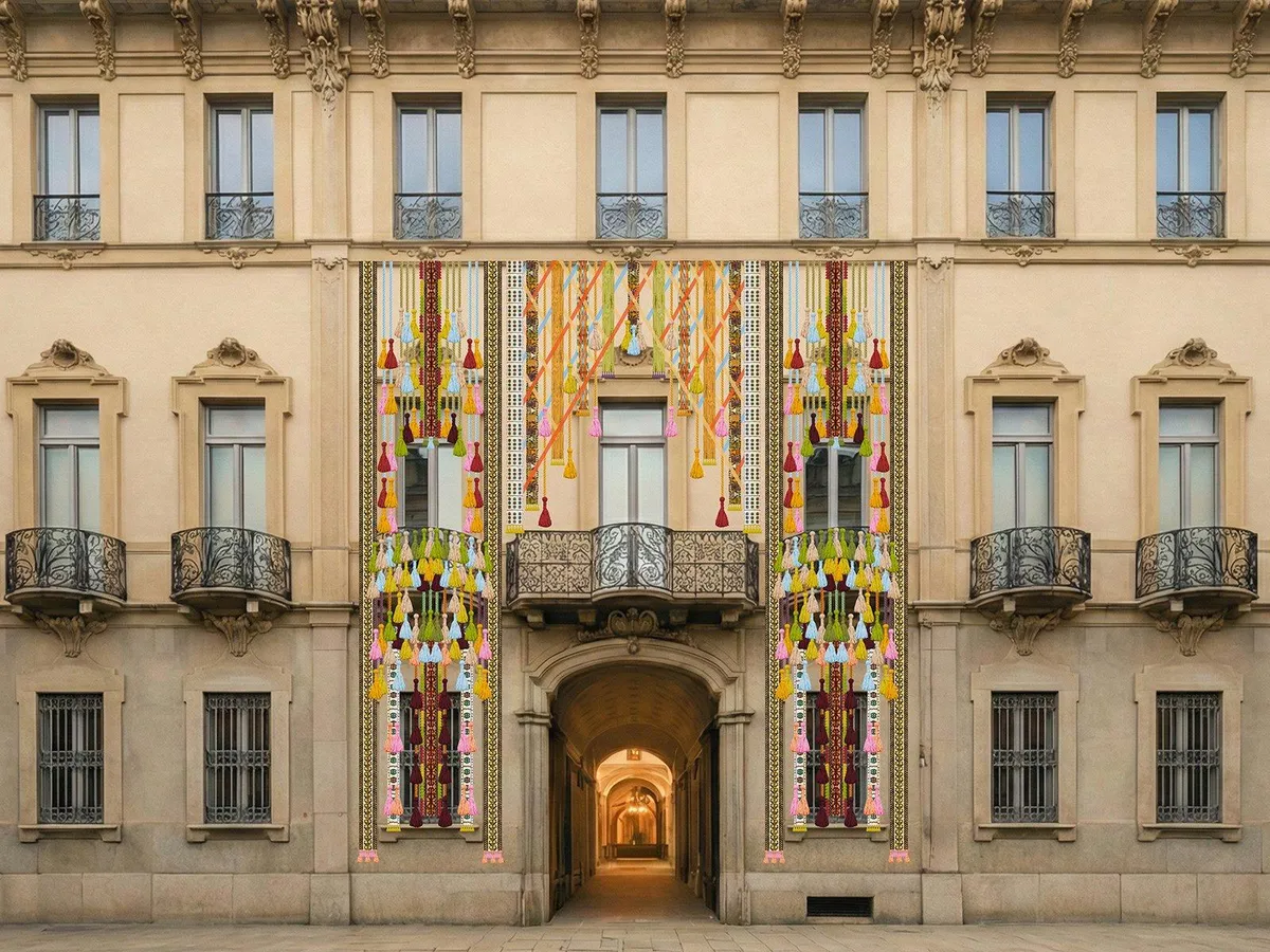 Milano Design Week 2026 kapsamında Özbekistan Kültür ve Geliştirme Vakfı tarafından hazırlanan, kemerli bir girişin ve iki balkonun bulunduğu bej rengi, süslü bir bina cephesine asılmış, sarı, kırmızı, yeşil, mavi ve pembe gibi canlı tonlarda çok sayıda püskül ve geleneksel desenlerle bezeli, göz alıcı When Apricots Blossom enstalasyonu.