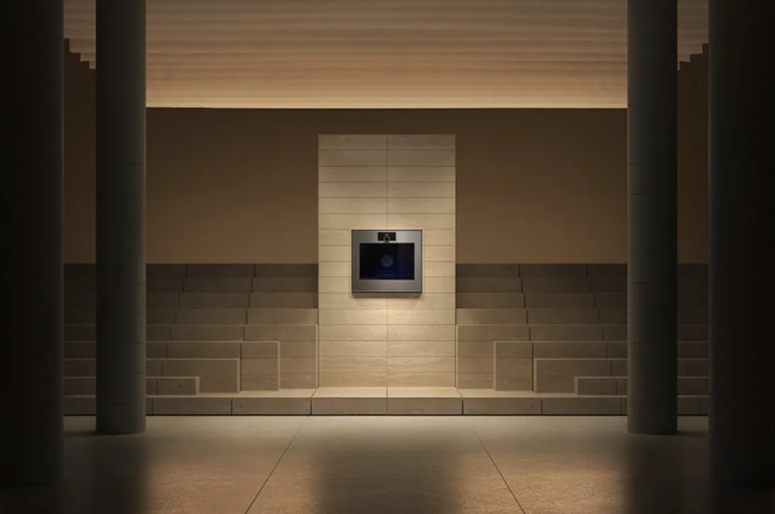 Ortasında modern bir Gaggenau cihazının minimalist taş duvar paneline entegre edildiği, iki yanında kademeli basamaklar ve loş ışıklı sütunların eşlik ettiği bu rafine mimari kurgu, Milano Design Week'te lüks teknoloji ve tasarımın sunduğu varlık deneyimini vurguluyor.