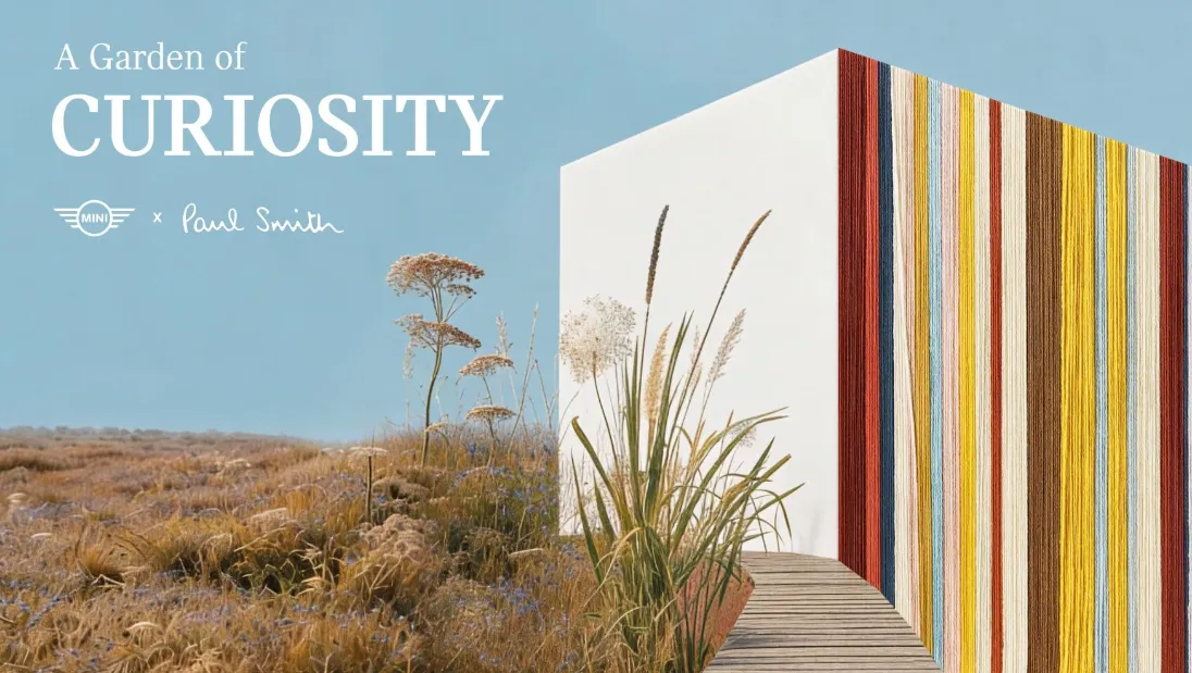 Milano Design Week 2026 kapsamında sergilenen MINI ve Paul Smith iş birliğindeki Merak Bahçesi enstalasyonundan bir görünüm; kuru otların ve uzun sazlıkların çevrelediği ahşap bir yürüyüş yolunun, bir yüzü Paul Smith’in imza niteliğindeki renkli çizgili ipliklerle kaplı beyaz bir yapıya doğru kıvrıldığı, gökyüzünün açık mavi olduğu sakin bir atmosferi betimliyor.