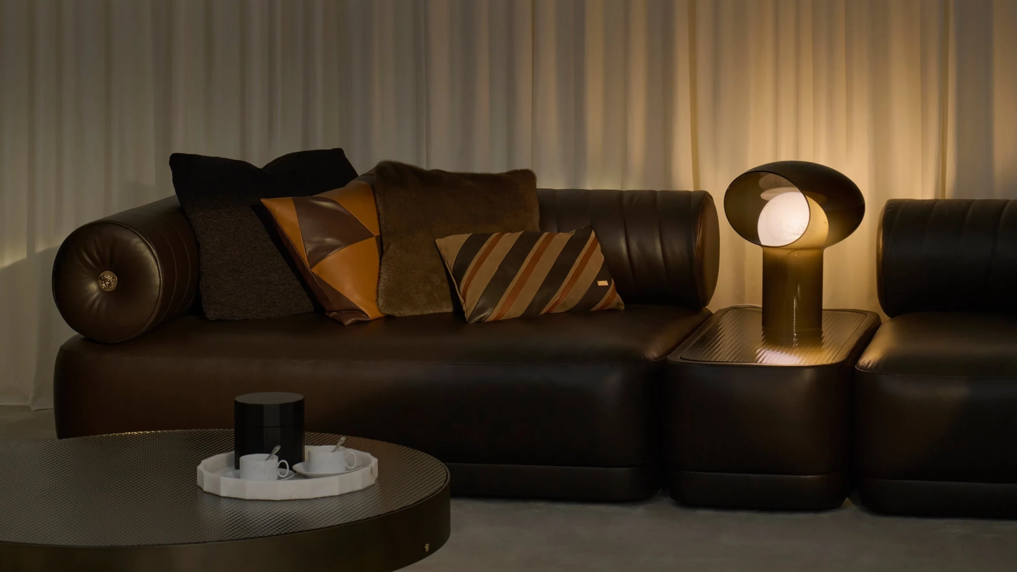 Koyu kahverengi deri kanepenin kolçağındaki altın Medusa amblemiyle dikkat çeken lüks Versace ev koleksiyonuna ait bu modern yaşam alanı, Milano Design Week'te sergilenen sofistike tasarım ve geleceğin yaşam formlarına dair çarpıcı bir örnek sunuyor.