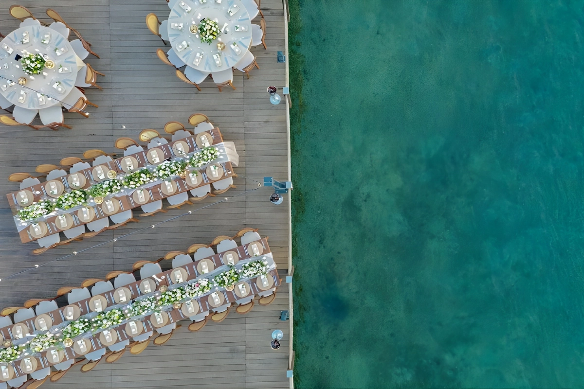 Mivara Luxury Resort & Spa Bodrum'da, masmavi Ege Denizi'nin kıyısında, zarif beyaz ve yeşil çiçek aranjmanlarıyla süslenmiş uzun ve yuvarlak masaların kuşbakışı göründüğü bu eşsiz manzara, Türk Rivierası'nda unutulmaz düğün deneyimleri için ideal bir mekan sunuyor.