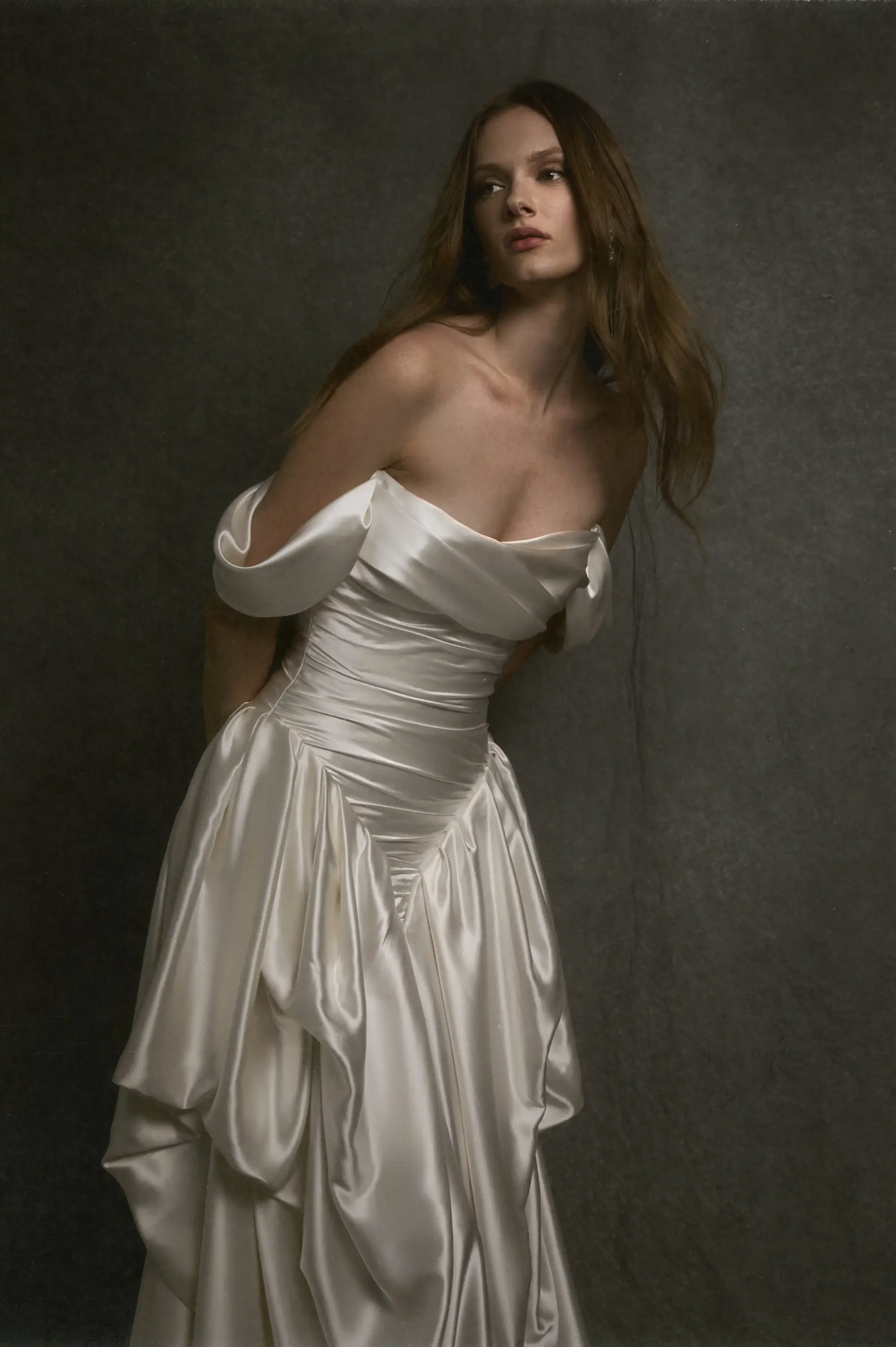 Uzun kahverengi saçları ve zarif duruşuyla model, New York Bridal Moda Haftası'nın öne çıkan trendlerinden olan Elie Saab 2027 İlkbahar Bridal koleksiyonundan, omuzları açıkta bırakan, zarif drapeli parlak fildişi rengi saten kumaşla tasarlanmış heykelsi ve romantik gelinliği sergiliyor.