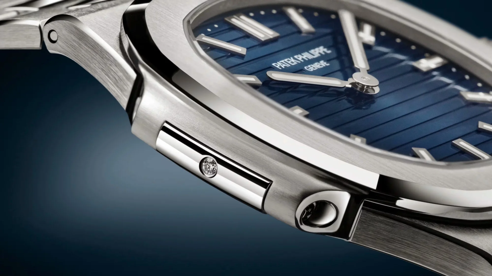 Yakın çekim, fırçalanmış ve parlak gümüş renkli metal Patek Philippe saatinin, koyu mavi çizgili kadranının ve kasasında parlayan tek bir pırlanta detayının zarif görünümünü sunuyor, 50. yıl özel serisinin estetiğini öne çıkarıyor.