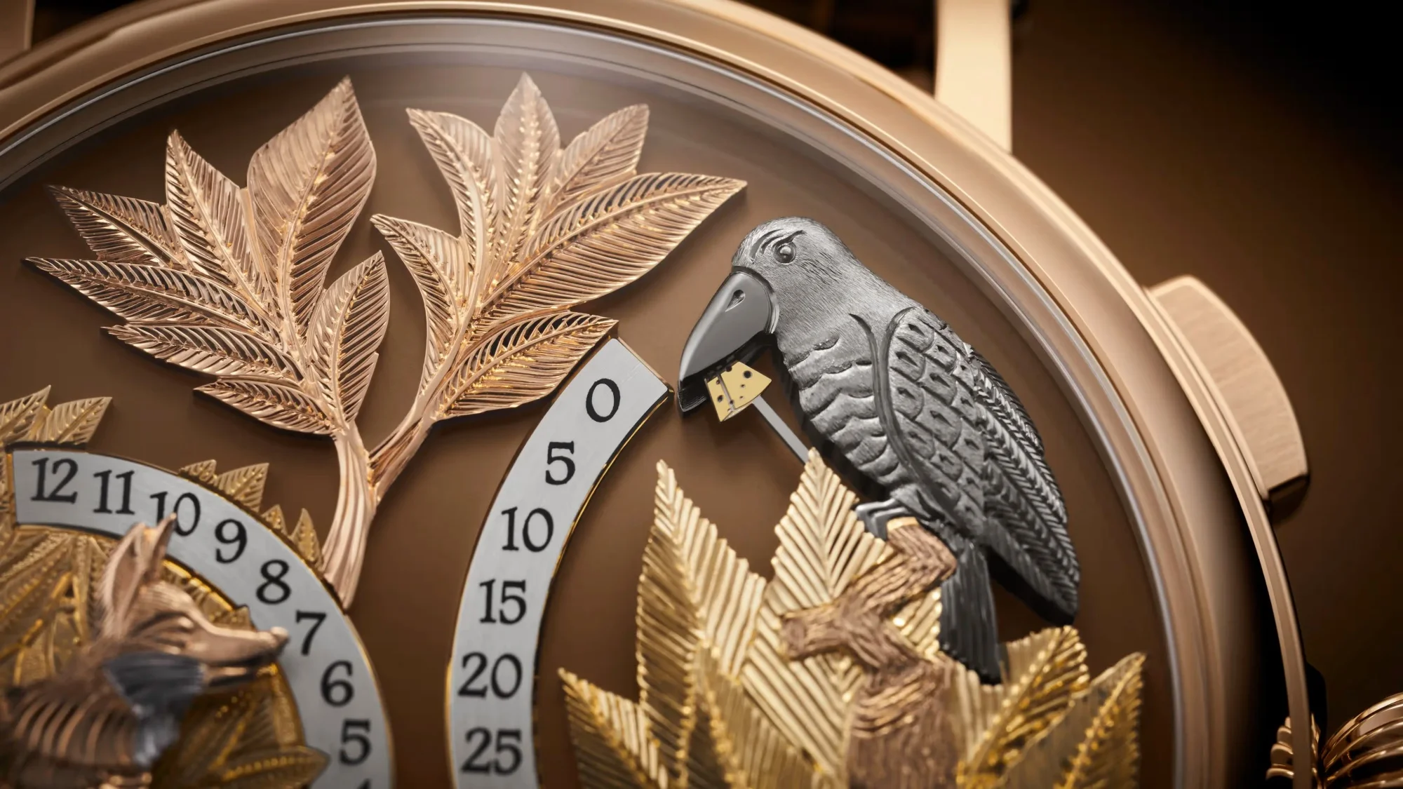 Watches and Wonders'ta tanıtılan Patek Philippe Calatrava Automaton 5249R modelinin eşsiz kadran detayında, kahverengi zeminde altın renkli yaprak işlemeleriyle süslenmiş bir orman teması içinde, gagasında sarı bir peynir parçası tutan hareketli gri bir papağan figürü ve alt bölümde görünen bir tilki heykeli, zengin el işçiliğini ve otomatik mekanizmayı vurguluyor.