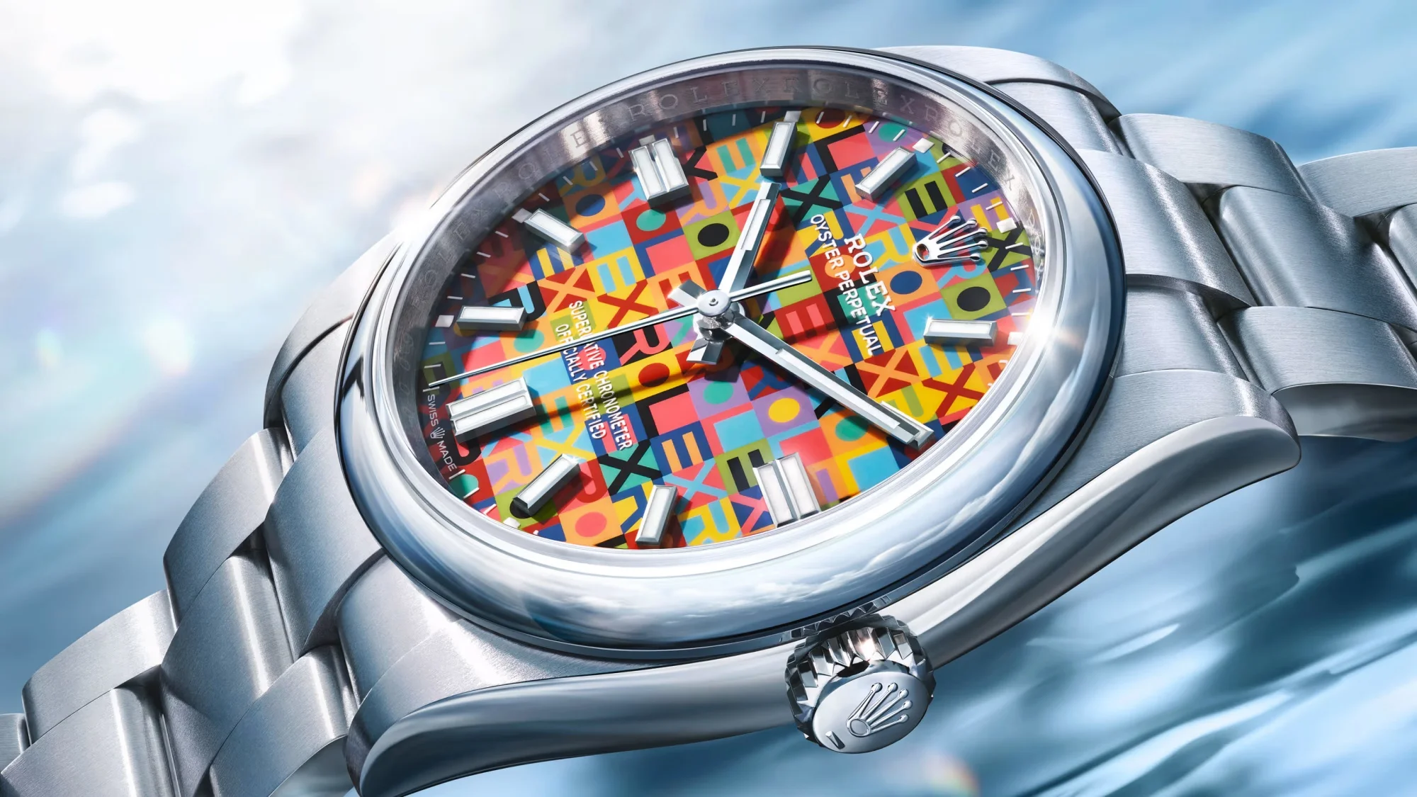 Yakın çekim bir fotoğraf, canlı renkli ve mozaik desenli kadranıyla dikkat çeken, parlak paslanmaz çelik kasa ve bileziğe sahip bir Rolex Oyster Perpetual 36 saati, Watches and Wonders etkinliğindeki yenilikleri yansıtan modern estetiğiyle gösteriyor.