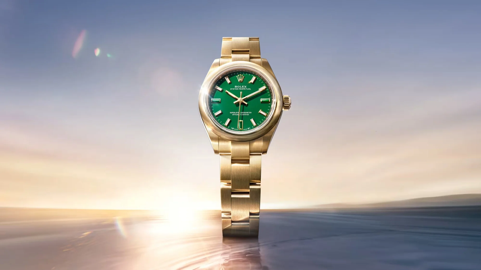 Huzurlu bir günbatımı veya gün doğumu ufuk çizgisi önünde parlayan, karakteristik yeşil kadrana sahip, zarif ve lüks bir Rolex Oyster Perpetual sarı altın kol saati, Watches and Wonders etkinliğinin dikkat çekici yeniliklerinden biri olarak öne çıkıyor.