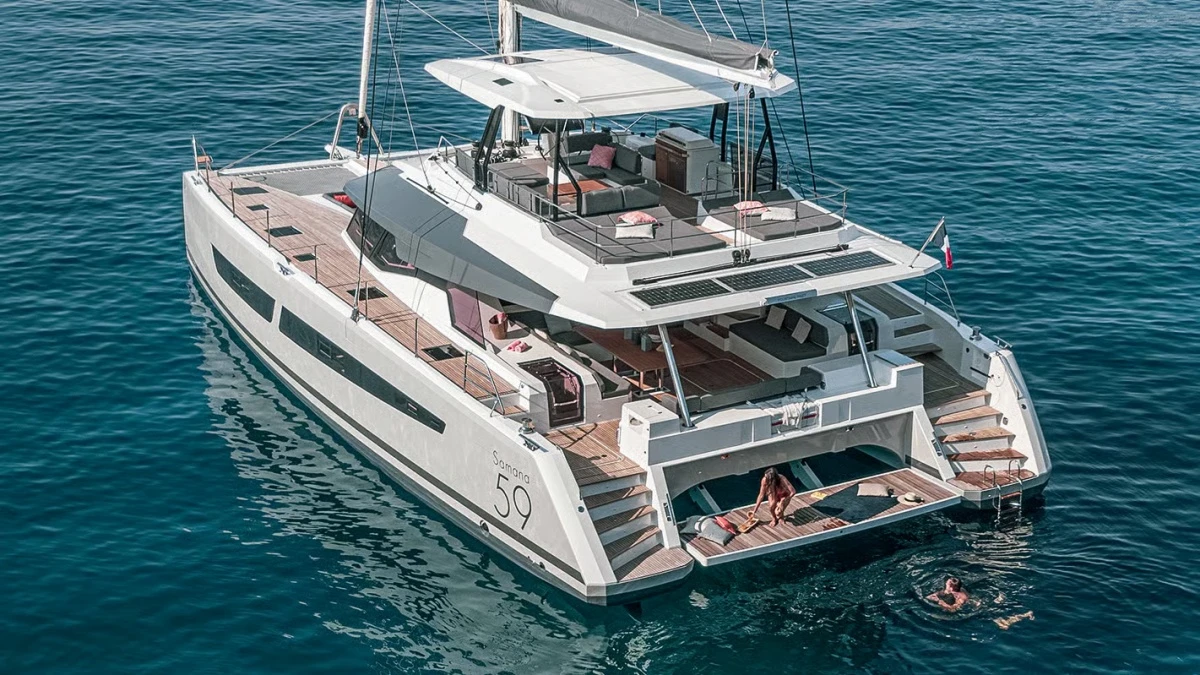 Mavi sularda yüzen, arka platformunda yüzmeye hazırlanan bir kadının ve suda yüzen bir kişinin görüldüğü, Fountaine Pajot tasarımı Samana 59 lüks katamaran yatın geniş açılı görünümü, Singapur Yat Fuarı'ndaki modern tekne deneyimini çağrıştırıyor.