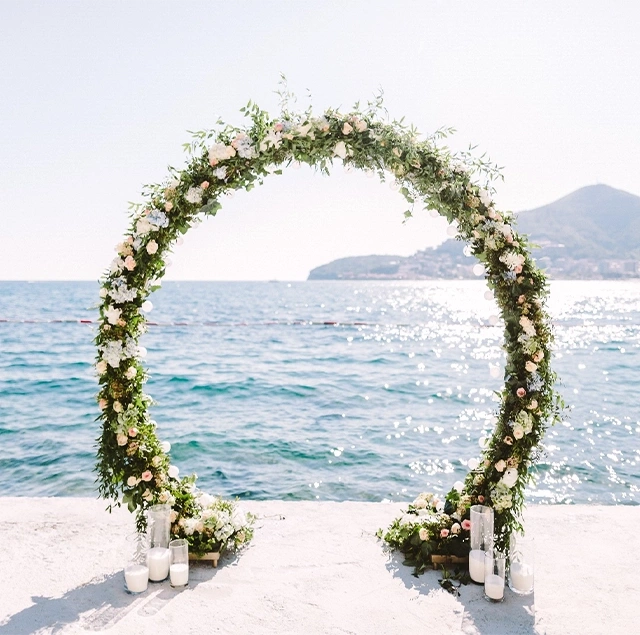 Bodrum'da unutulmaz bir düğün deneyimi sunan, deniz kenarındaki bir iskelede, çiçeklerle bezenmiş zarif yuvarlak nikah takı ve etrafındaki mumlar, berrak Ege Denizi manzarası eşliğinde romantik bir atmosfer yaratıyor.