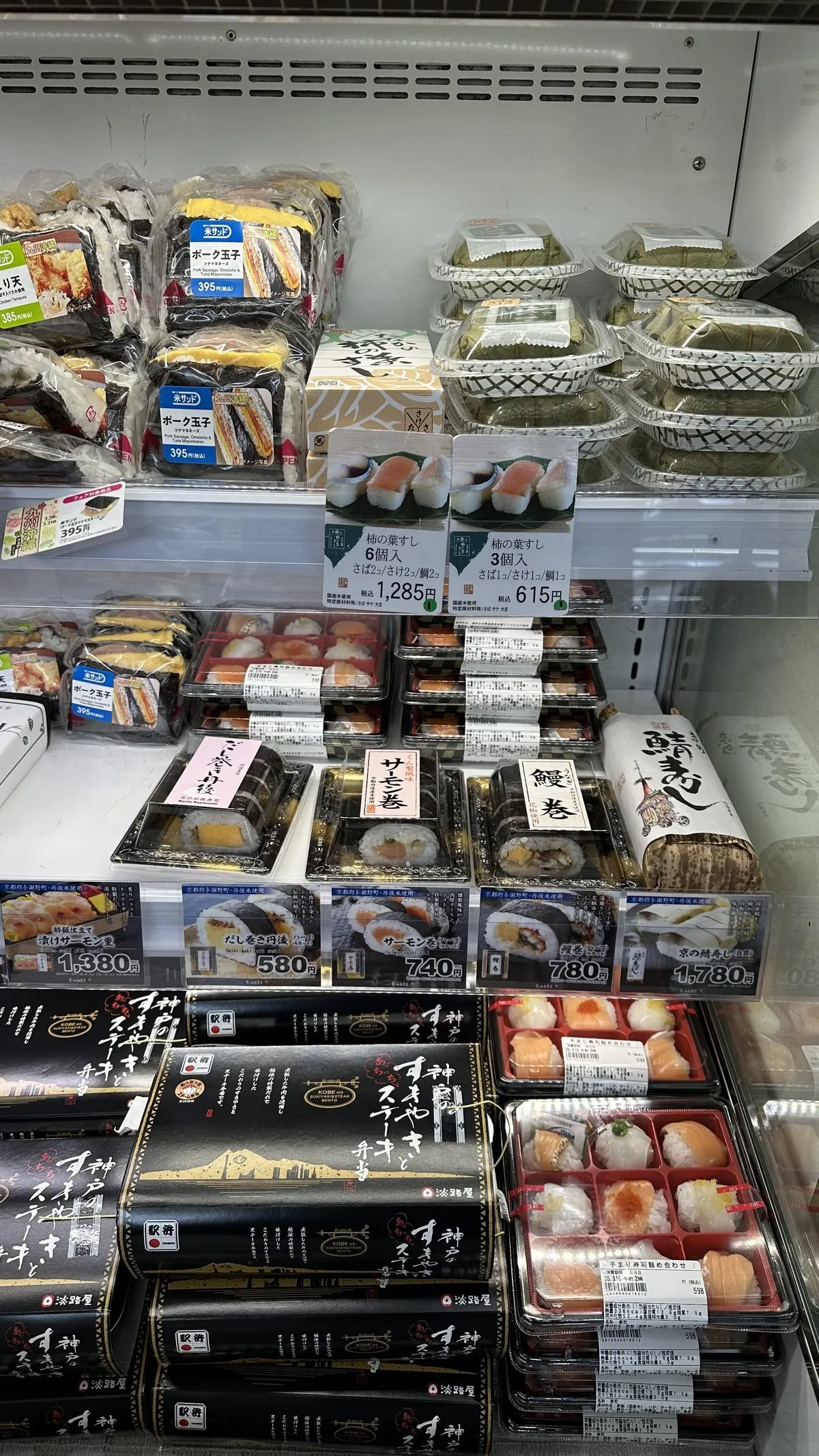 Tokyo'daki bir süpermarketin soğutuculu rafında, çeşitli içeriklere sahip onlarca paketlenmiş bento kutusu, sushi setleri ve onigiri topları dikkat çekici fiyat etiketleriyle düzenli bir şekilde sergileniyor.