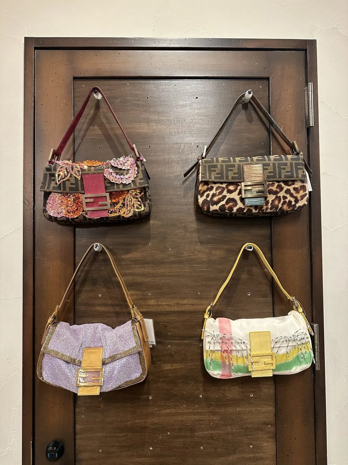 Koyu renkli ahşap bir kapı üzerinde sergilenen bu özel dört Fendi Baguette çanta, leopar desenli, pullu çiçek işlemeli, mor payetli ve renkli çizgili gibi farklı doku ve desenleriyle Tokyo'daki vintage moda ruhunu yansıtıyor.
