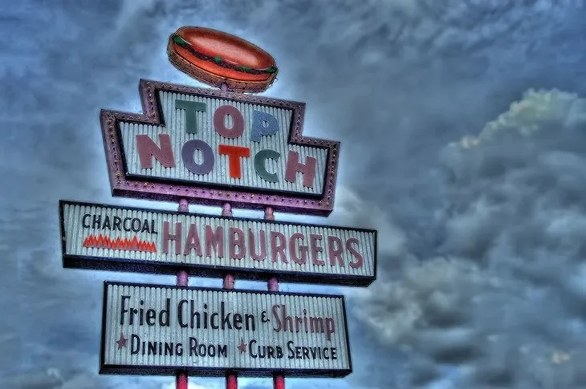Bulutlu gökyüzünün altında parlayan, Richard Linklater'ın kült filmi Dazed and Confused'da gençlerin buluşma noktası olarak filmlerde geçen ünlü Top Notch Hamburgers restoranının retro neon tabelası, üzerinde hamburger görseli, Charcoal Hamburgers, Fried Chicken & Shrimp ve Dining Room & Curb Service ibarelerini çok katmanlı yapısıyla sergiliyor.