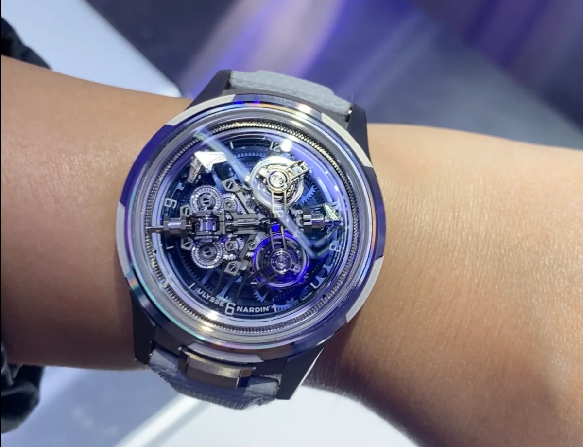 Bir bilekte yakından sergilenen, metal kasası ve gri kayışıyla zarif duran, karmaşık açık mekanizmasını ve parlayan mavi detayları gözler önüne seren, Ulysse Nardin Super Freak model lüks saat, mekanik şaheserlere olan hayranlığı artırıyor.
