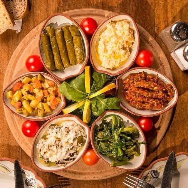 Ahşap bir tepsi üzerinde, ortasında taze yeşillikler ve limon dilimleri ile süslenmiş, yaprak sarma, haydari, acılı ezme, zeytinyağlı otlar ve çeşitli salatalar gibi altı farklı Ege mezesi, Urla'nın özgün tatlarını ve bölgenin en iyi mekanlarında sunulan zengin mutfağını vurguluyor.