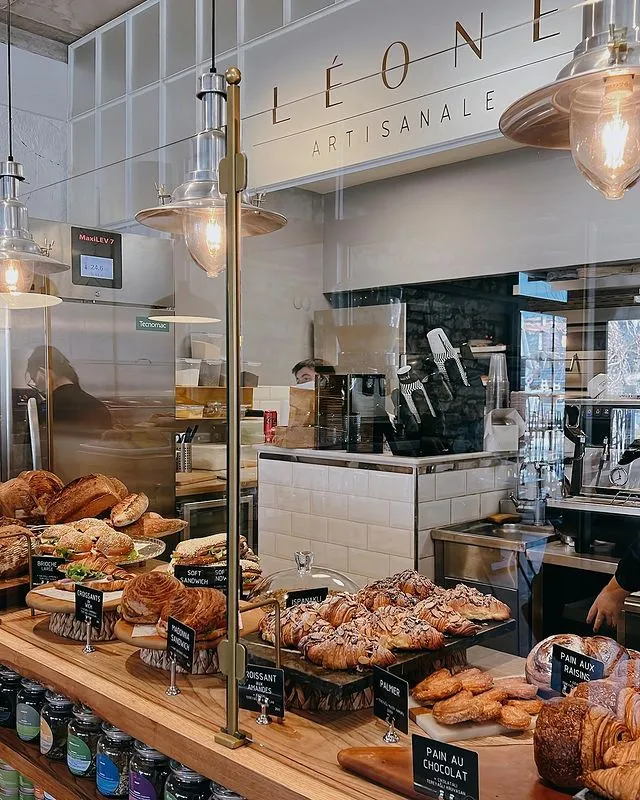 Urla'nın en lezzetli mekanlarından Léone Artisanale'de, modern ve aydınlık bir kafenin ahşap tezgahı üzerinde özenle sergilenen bademli kruvasanlar, farklı sandviçler, pain au chocolat ve çeşitli ekmekler gibi taze fırın ürünleri ağız sulandıran bir görünüm sunuyor.