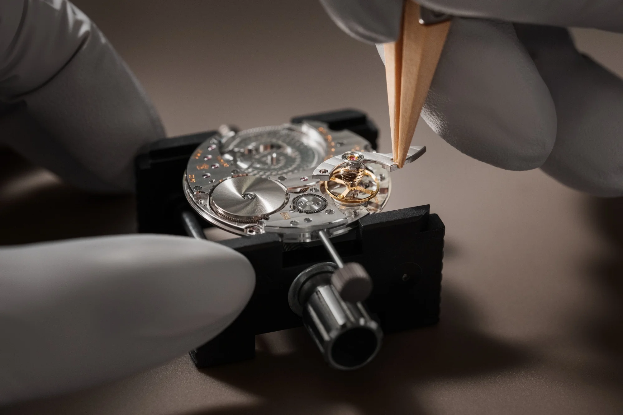 Eldivenli ellerin cımbızla, Vacheron Constantin'in karmaşık otomatik kurmalı mekanizmasının hassas parçalarını titizlikle bir araya getirdiği bu yakın çekim, üst düzey saatçiliğin detay işçiliğini ve mükemmeliyet arayışını vurguluyor.