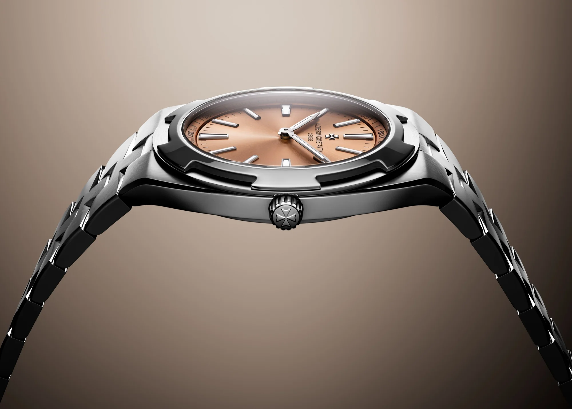 Vacheron Constantin Overseas Ultra-Thin modelinin zarif inceliğini vurgulayan bu yandan çekimde, parlak paslanmaz çelik kasa ve entegre bileziği ile canlı somon kadranı öne çıkarken, kurma kolundaki Malta haçı logosu markanın imzası niteliğindedir.