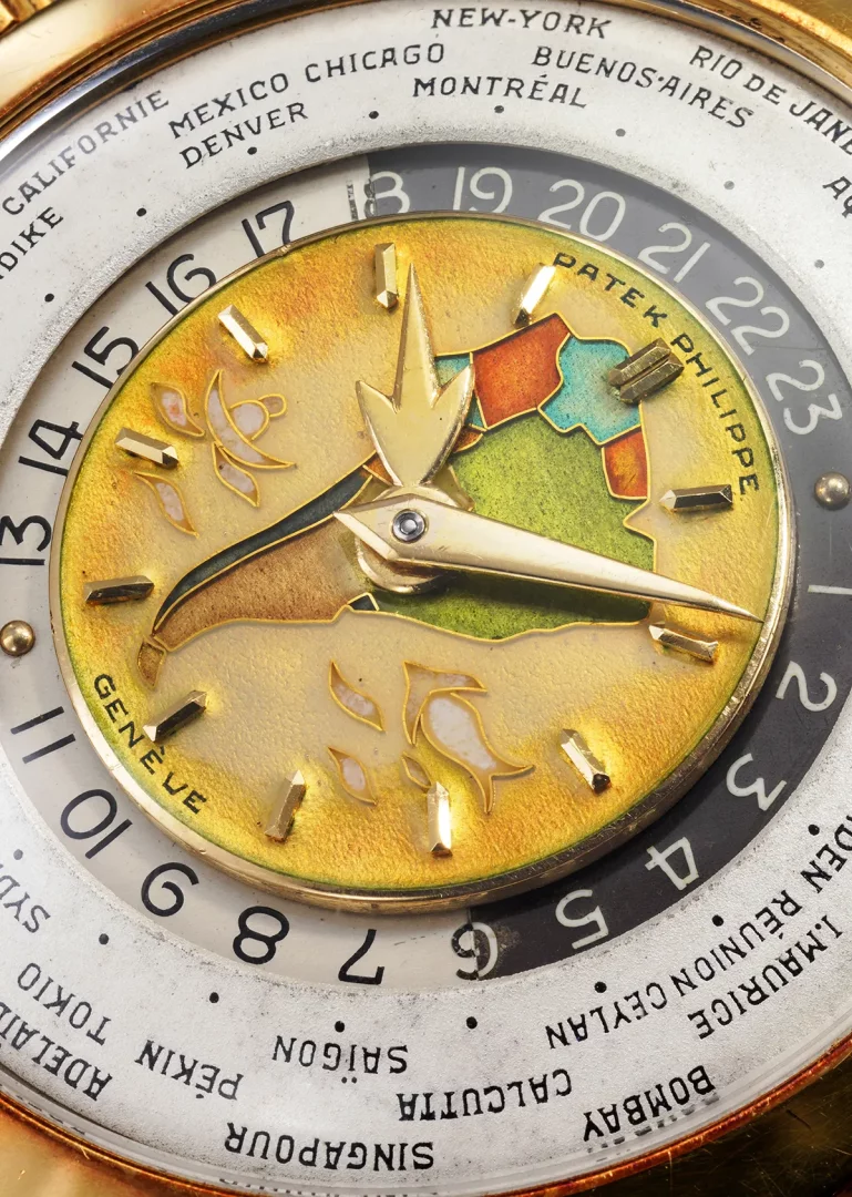 Yakın çekimdeki bu Patek Philippe dünya saati kadranı, ortasında altın tonlarında emaye dünya haritası deseni ve zarif ibreleriyle dikkat çekerken, dış halkasında New York, Cenevre gibi şehir adları ve 24 saatlik zaman dilimleri ustaca gösterilerek küresel zamanı takip etmeyi sağlar.
