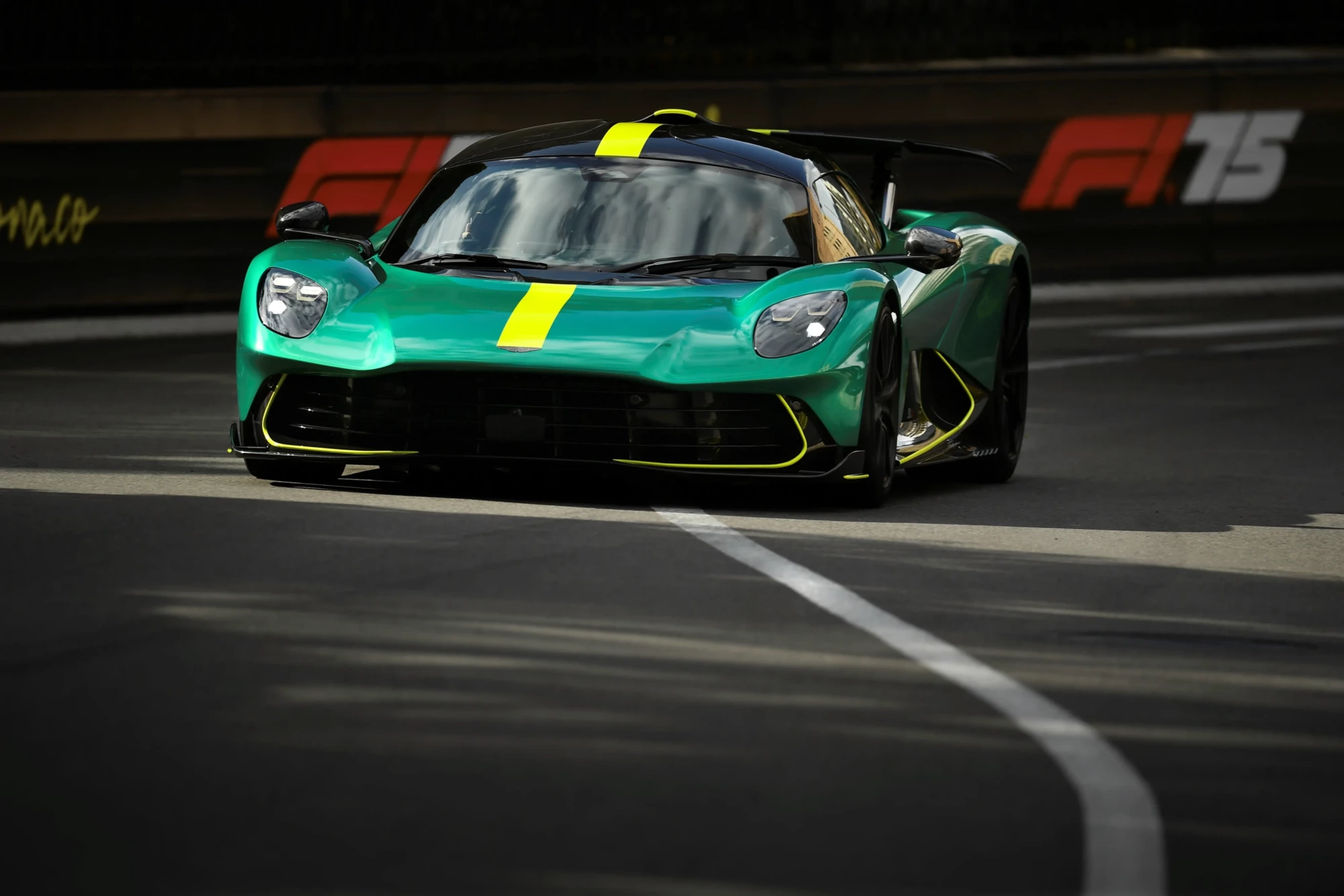 Parlak zümrüt yeşili renkte ve üzerinde sarı bir yarış şeridi bulunan Aston Martin Valhalla, Formula 1 teknolojisinden ilham alan aerodinamik tasarımıyla Monaco pistinde viraj alırken dinamik bir şekilde önden görülüyor.