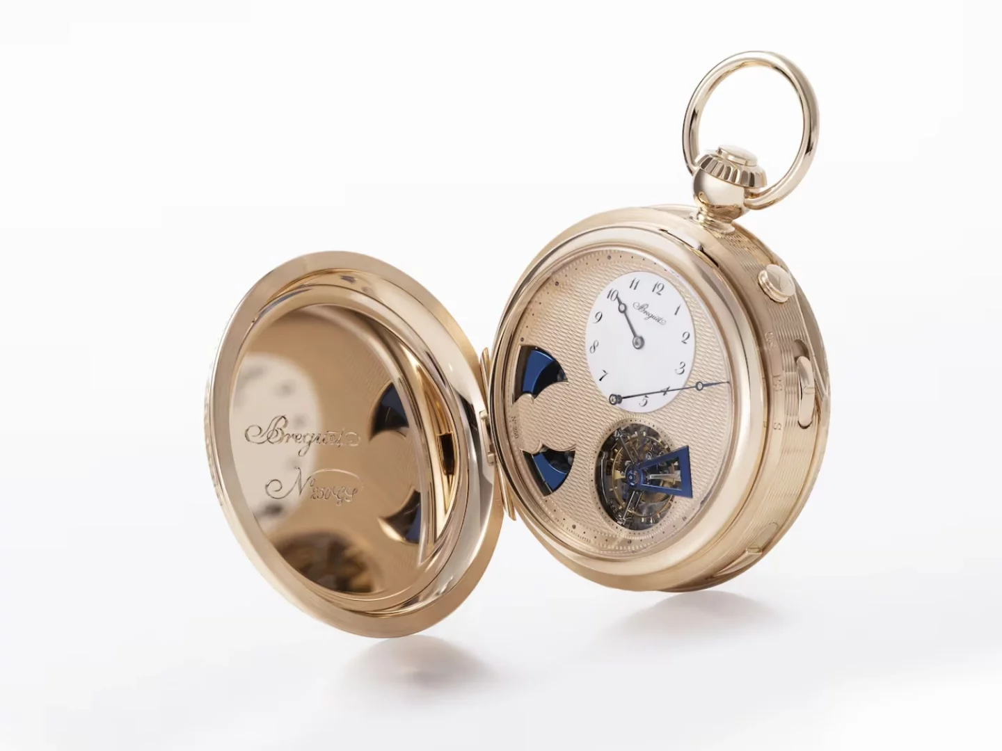 Beyaz fon üzerinde açık duran, altın rengi, kapağında Breguet N° 1905 gravürü bulunan bu Métiers d'Art Breguet cep saati, karmaşık guilloché kadranı, hassas mavi detaylara sahip mekanizması ve zarif beyaz alt kadranıyla saatçilik sanatını gözler önüne seriyor.